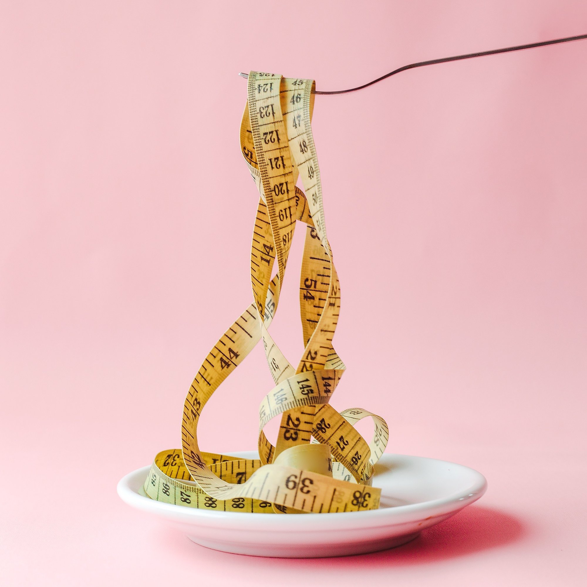 fork-lifting-yellow-measuring-tape-swirls-white-plate-isolated-pink-background-1